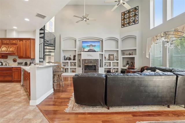 living room with built in features, a high ceiling, ceiling fan, and light tile floors