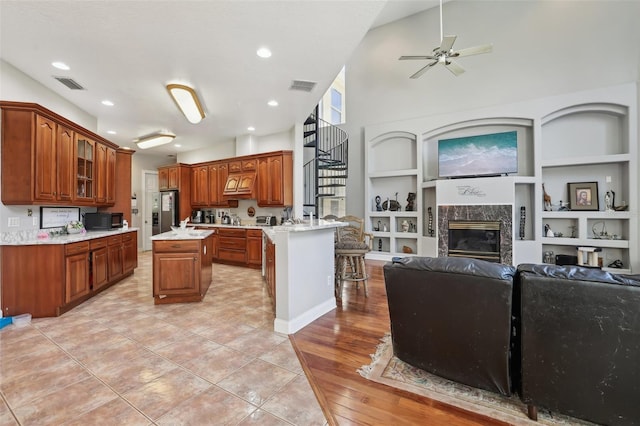 kitchen featuring ceiling fan, a fireplace, built in features, light tile floors, and a breakfast bar