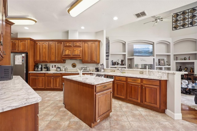 kitchen featuring an island with sink, ceiling fan, light tile flooring, and stainless steel refrigerator