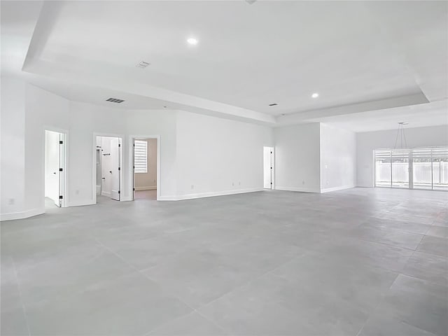 empty room featuring a raised ceiling, recessed lighting, baseboards, and visible vents