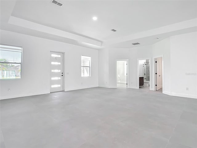 unfurnished living room with visible vents, a healthy amount of sunlight, and a raised ceiling