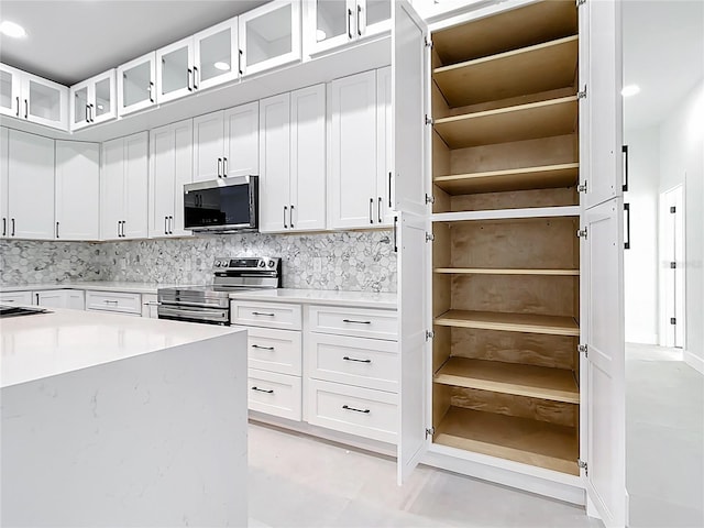 kitchen featuring stainless steel appliances, glass insert cabinets, tasteful backsplash, and white cabinetry