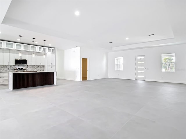 unfurnished living room with recessed lighting, a raised ceiling, plenty of natural light, and finished concrete flooring