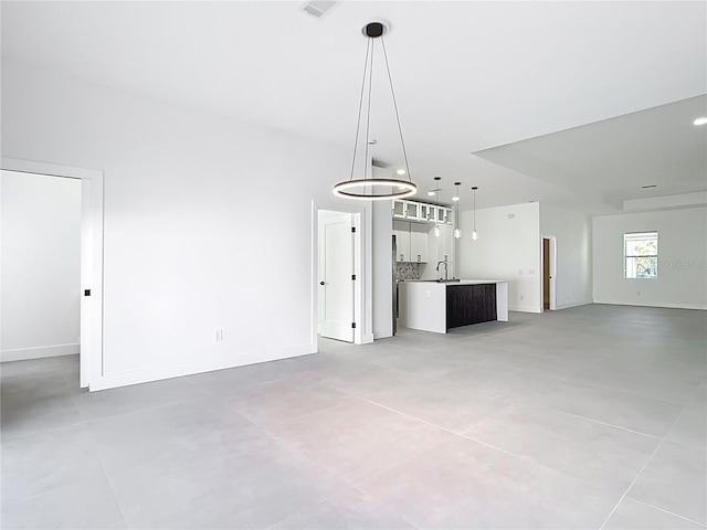 unfurnished living room with baseboards, a chandelier, and a sink