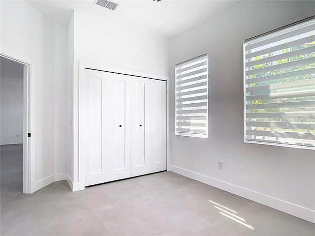 unfurnished bedroom with visible vents, baseboards, concrete floors, and a closet