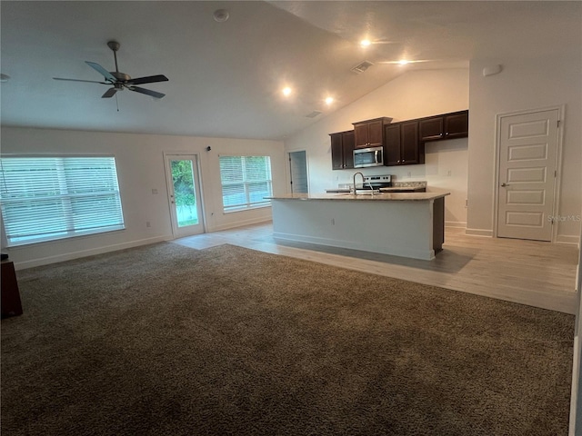 kitchen with an island with sink, ceiling fan, vaulted ceiling, and light colored carpet