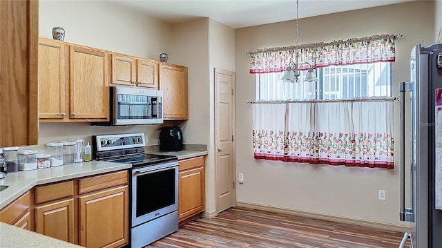 kitchen with stainless steel appliances, hardwood / wood-style flooring, and pendant lighting