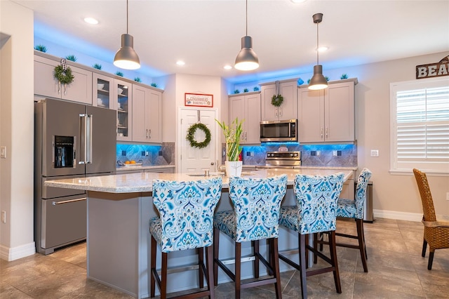 kitchen with gray cabinets, appliances with stainless steel finishes, a kitchen island with sink, and decorative light fixtures