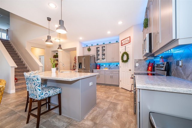 kitchen with sink, pendant lighting, stainless steel appliances, light stone countertops, and a kitchen island with sink