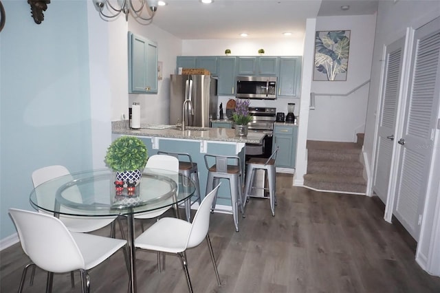 kitchen featuring kitchen peninsula, a kitchen breakfast bar, light stone counters, stainless steel appliances, and dark wood-type flooring