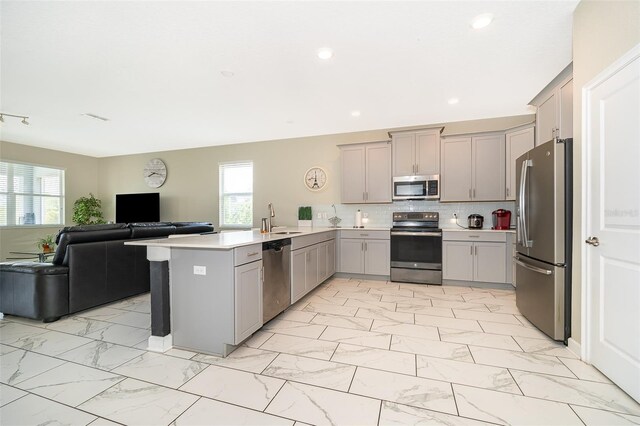 kitchen with sink, kitchen peninsula, gray cabinets, decorative backsplash, and appliances with stainless steel finishes