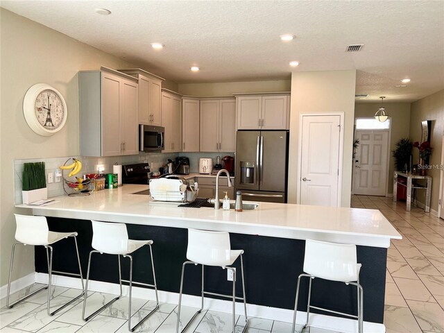 kitchen featuring kitchen peninsula, appliances with stainless steel finishes, a kitchen breakfast bar, sink, and gray cabinets