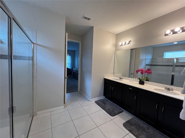 bathroom with tile patterned floors, vanity, a shower with door, and a textured ceiling