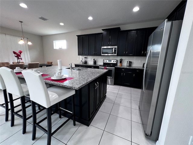 kitchen with an inviting chandelier, a kitchen breakfast bar, light stone countertops, an island with sink, and appliances with stainless steel finishes