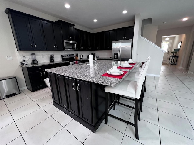 kitchen featuring light stone countertops, sink, stainless steel appliances, a kitchen island with sink, and a breakfast bar