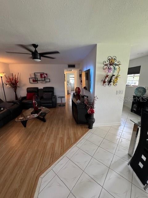 living room with ceiling fan, a textured ceiling, and light tile floors