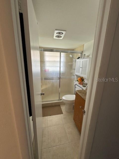 bathroom with tile flooring, an enclosed shower, vanity, and toilet