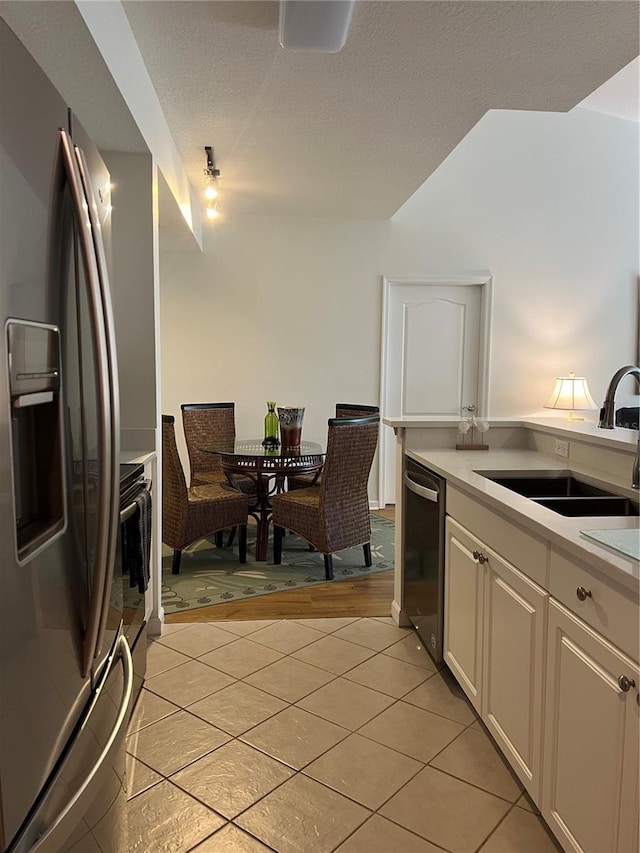 kitchen with white cabinets, sink, light tile patterned floors, a textured ceiling, and appliances with stainless steel finishes