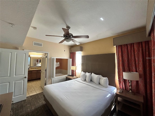 bedroom featuring ceiling fan, ensuite bathroom, light tile patterned floors, and a textured ceiling