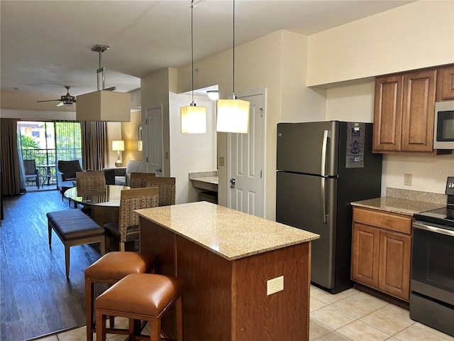 kitchen with pendant lighting, light hardwood / wood-style flooring, ceiling fan, appliances with stainless steel finishes, and a kitchen island