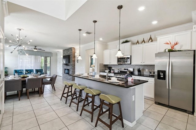 kitchen featuring ceiling fan with notable chandelier, a kitchen breakfast bar, an island with sink, white cabinetry, and stainless steel appliances