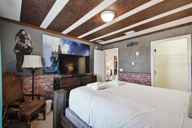 bedroom with a walk in closet, carpet floors, and brick wall