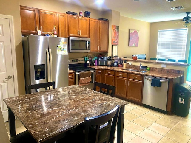 kitchen with kitchen peninsula, appliances with stainless steel finishes, sink, light tile patterned floors, and dark stone countertops