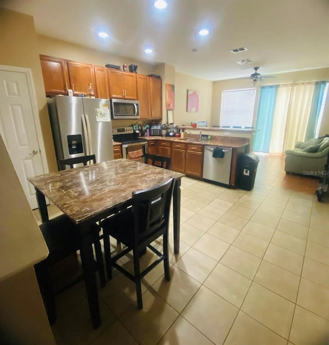 kitchen featuring ceiling fan, light tile patterned floors, a kitchen bar, kitchen peninsula, and stainless steel appliances