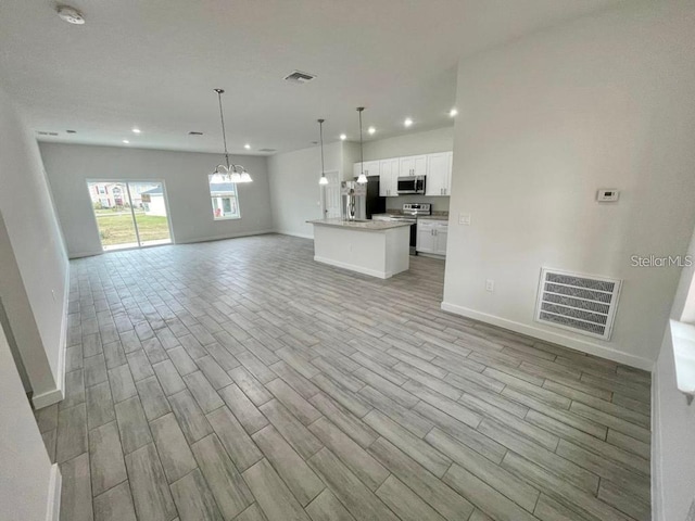 kitchen with pendant lighting, an inviting chandelier, white cabinets, appliances with stainless steel finishes, and a kitchen island