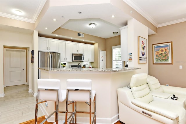 kitchen featuring a kitchen breakfast bar, white cabinetry, light stone counters, kitchen peninsula, and stainless steel appliances