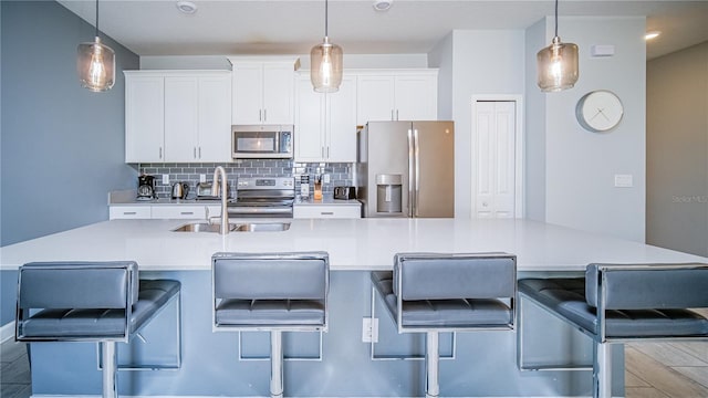 kitchen featuring a kitchen breakfast bar, a kitchen island with sink, stainless steel appliances, and decorative light fixtures