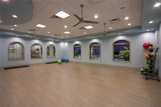 exercise area with ceiling fan, a drop ceiling, and light wood-type flooring