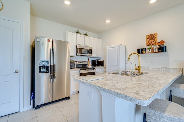 kitchen with sink, appliances with stainless steel finishes, a kitchen breakfast bar, white cabinets, and kitchen peninsula