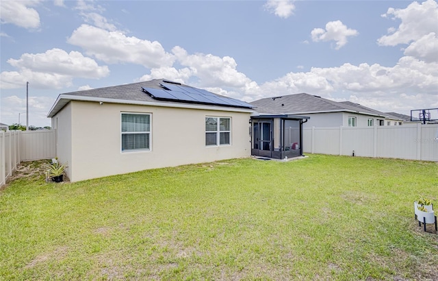 back of property with a lawn, a sunroom, and solar panels