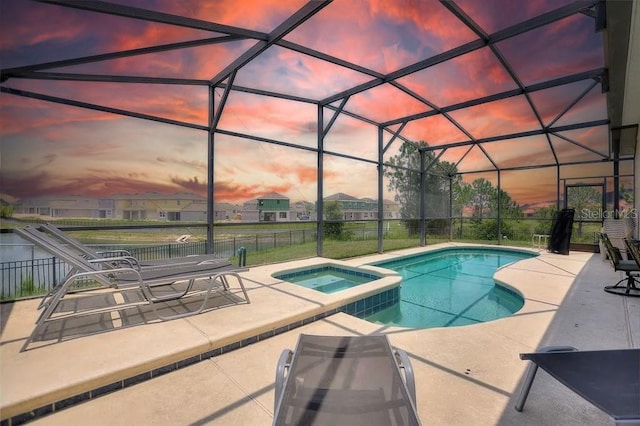 pool at dusk featuring glass enclosure, an in ground hot tub, and a patio