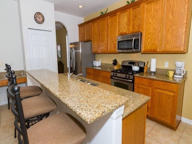 kitchen with light stone countertops, sink, appliances with stainless steel finishes, and an island with sink