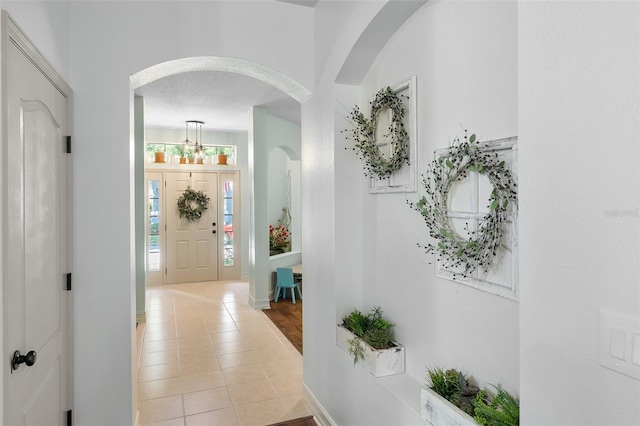 hall with light tile patterned flooring and an inviting chandelier