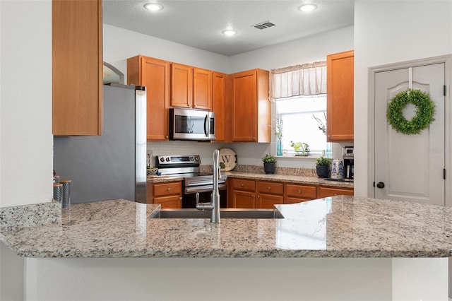 kitchen featuring kitchen peninsula, appliances with stainless steel finishes, and light stone counters