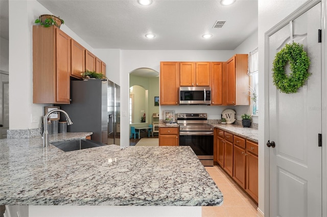 kitchen featuring kitchen peninsula, light stone counters, stainless steel appliances, sink, and light tile patterned floors