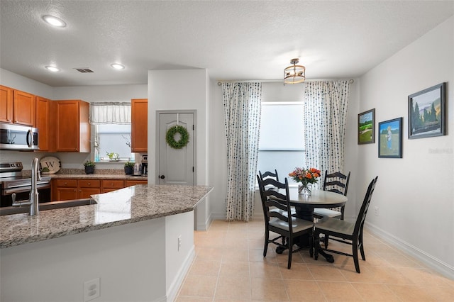 kitchen with light stone counters, light tile patterned flooring, a textured ceiling, and appliances with stainless steel finishes