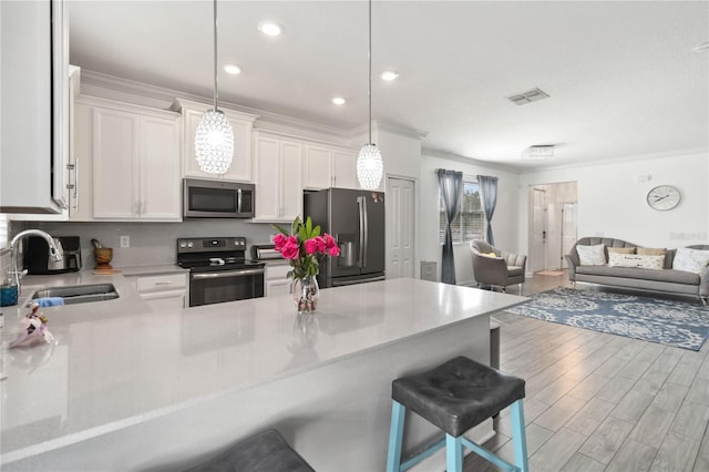 kitchen with sink, appliances with stainless steel finishes, white cabinetry, hanging light fixtures, and a kitchen breakfast bar