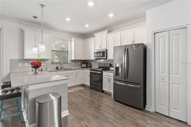 kitchen with a breakfast bar area, appliances with stainless steel finishes, hanging light fixtures, white cabinets, and kitchen peninsula