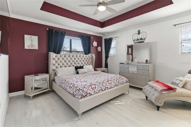 bedroom with crown molding, a tray ceiling, multiple windows, and light wood-type flooring