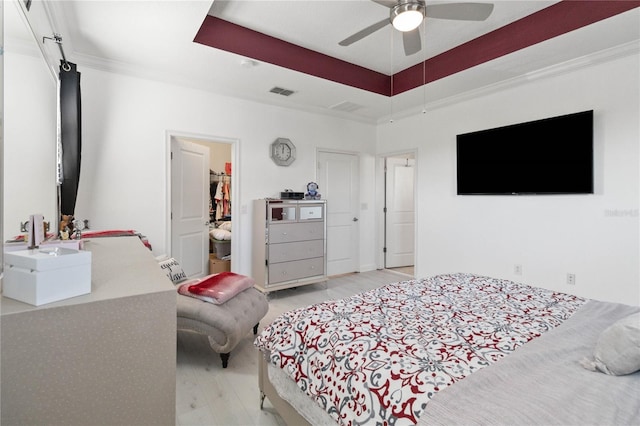 bedroom featuring a raised ceiling, ornamental molding, ceiling fan, and light wood-type flooring