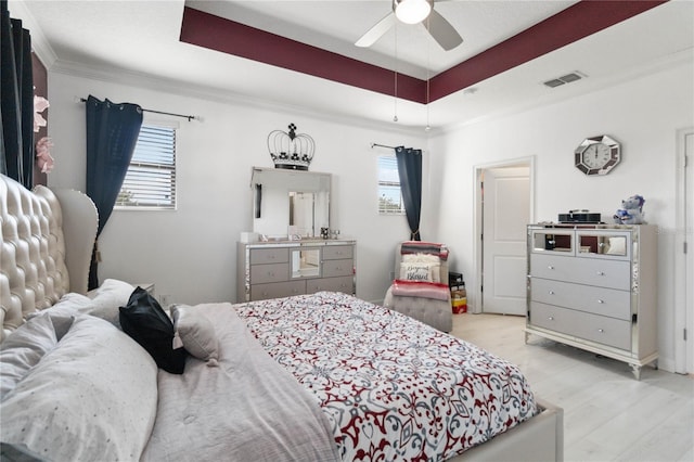 bedroom with a tray ceiling, ornamental molding, ceiling fan, and light wood-type flooring