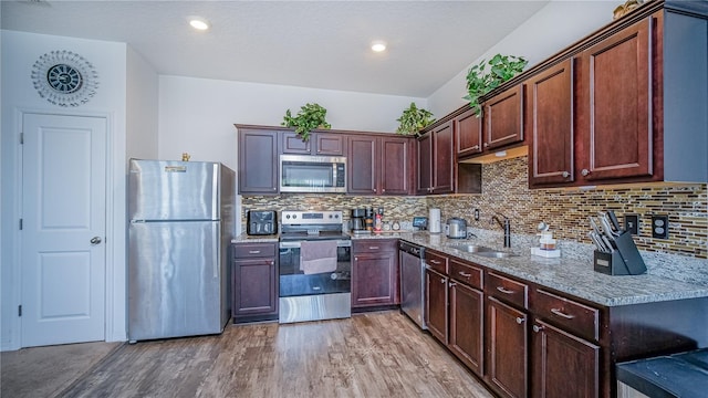 kitchen featuring sink, stainless steel appliances, light stone counters, light hardwood / wood-style floors, and decorative backsplash