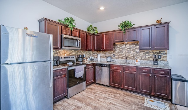 kitchen with sink, light stone countertops, appliances with stainless steel finishes, tasteful backsplash, and light hardwood / wood-style floors