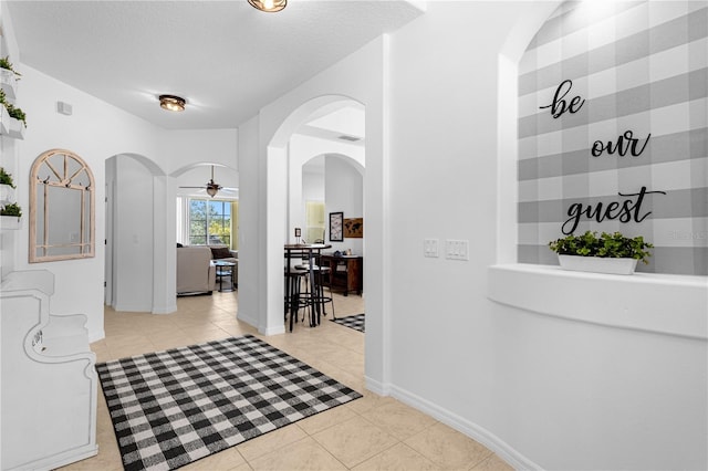 hall featuring arched walkways, light tile patterned floors, a textured ceiling, and baseboards