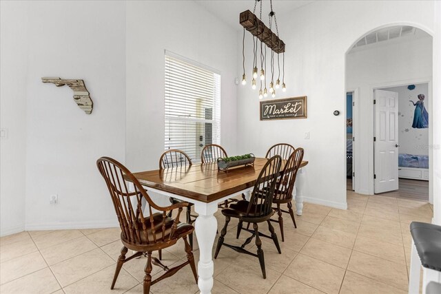 dining room featuring arched walkways, light tile patterned floors, visible vents, a high ceiling, and baseboards