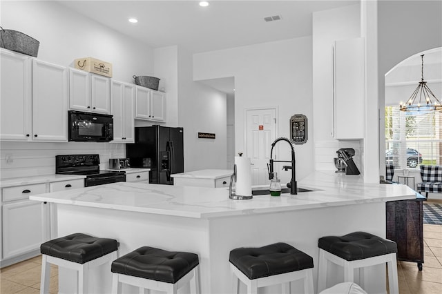 kitchen with black appliances, a breakfast bar area, a peninsula, and light stone countertops